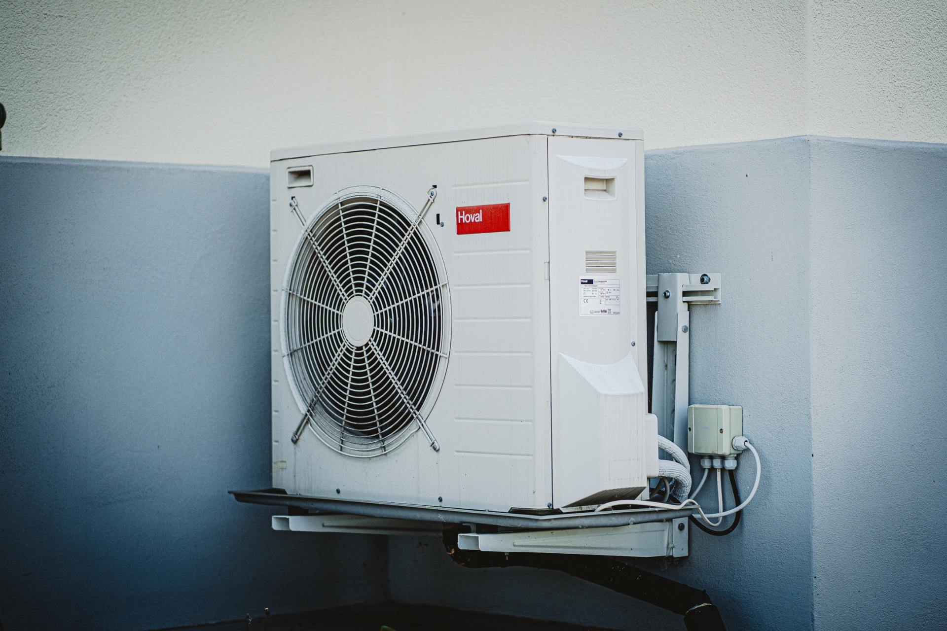 White air conditioning unit mounted on a gray wall, outdoor setting.
