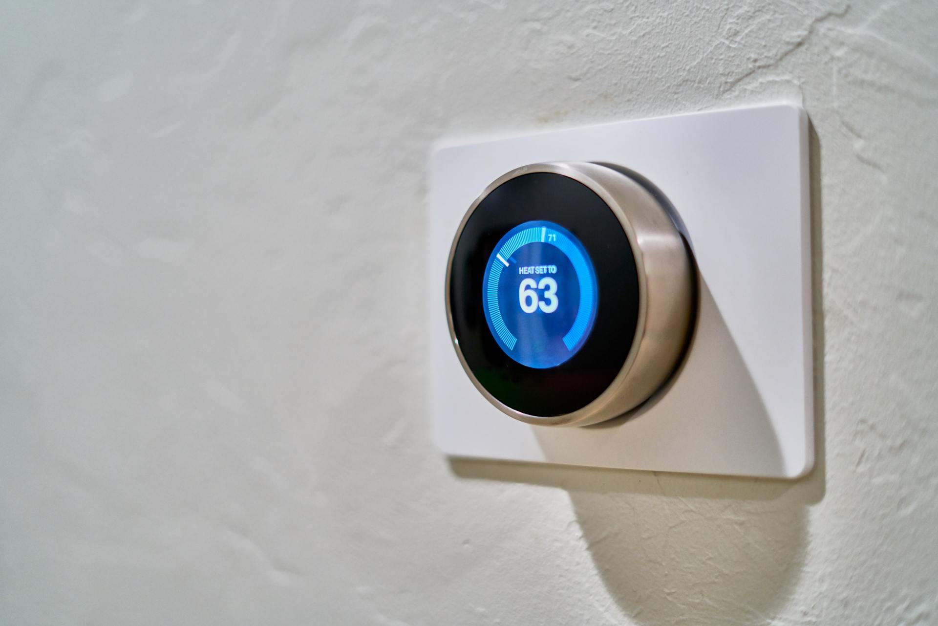 Smart thermostat on a white wall, displaying a temperature of 63 degrees.